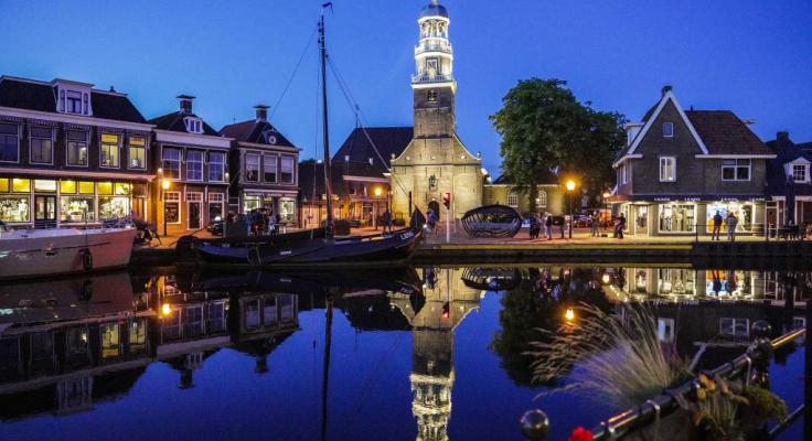 Avondzicht op Lemmer met verlichte toren en grachten, perfect voor Aqua-State vakantiehuisjes.